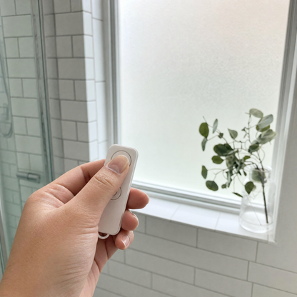 Hand pressing the Veilo remote with a frosted bathroom window behind
